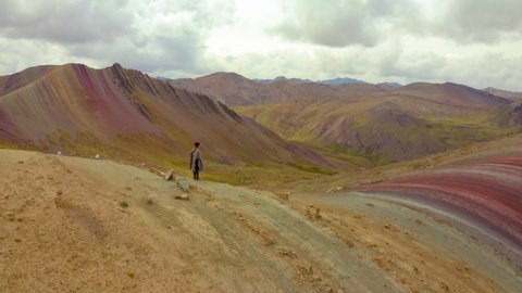 Aerial view of woman with arms outstretched running on mountain against cloudy sky, people on beautiful landscape - Rainbow Mountain, Peru