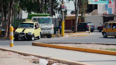 Slow motion panning shot of vehicles on street against trees in city during sunny day - Huacachina, Peru