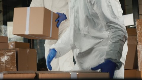 Men movers in protective suits load cardboard boxes with medicines into the car