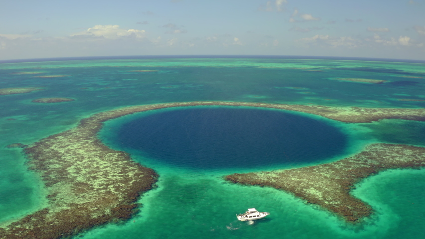 Aerial view of yacht near marine sinkhole on sunny day, drone panning from left to right over sea against sky - Great Blue Hole, Belize Royalty-Free Stock Footage #1051314436