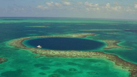 Aerial view of marine sinkhole with yacht against cloudy sky, scenic view of seascape with drone moving reversing from left to right - Great Blue Hole, Belize