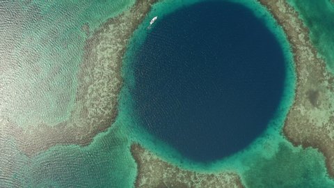 Aerial top view of yacht in famous marine sinkhole, seascape on sunny day while drone turning from right to light - Great Blue Hole, Belize