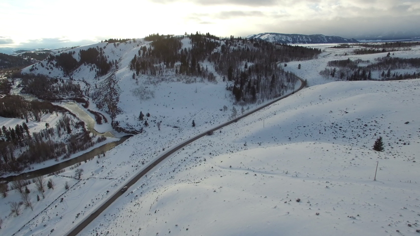 Aerial view of car on highway amidst snowcapped landscape, forest during winter against sky - Jackson, Wyoming