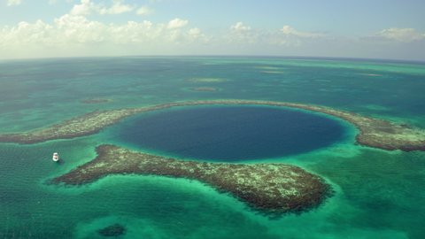 Aerial: Yacht near sinkhole against sky on sunny day, scenic view of seascape while drone panning from left to right - Great Blue Hole, Belize