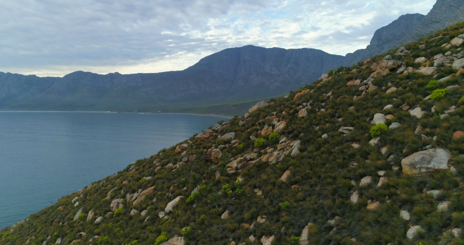 A striking aerial over cars driving down a long road ringing the shore of a large bay in South Africa - Cape Town, South Africa