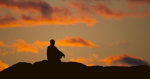 Monk is meditating on sunset sky background