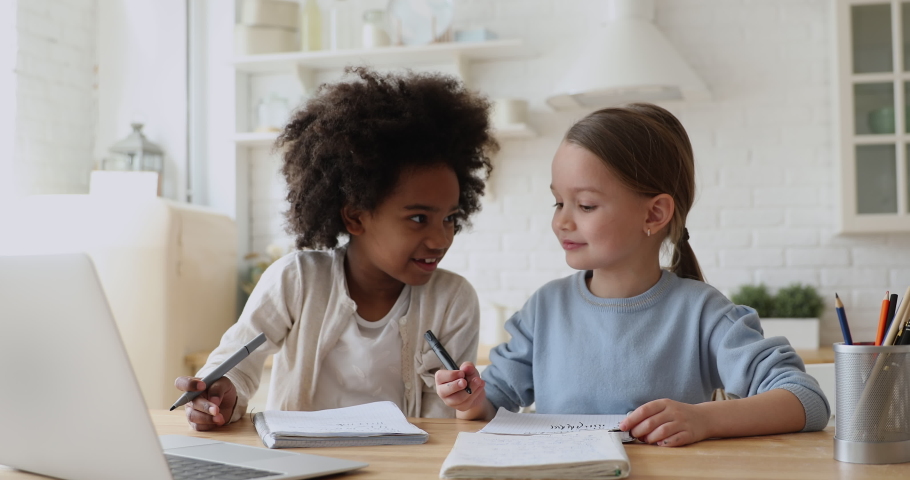 Happy cute afro american and caucasian kid girls having fun playing, talking, doing homework sitting at home table. Two mixed race ethnicity elementary school children friends studying together. | Shutterstock HD Video #1051329847