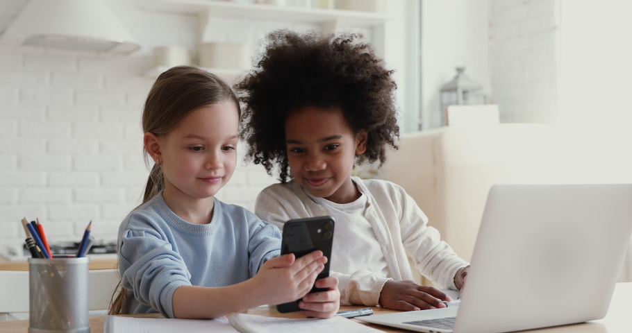 Two happy cute diverse ethnicity children using smartphone app for remote mobile education having fun playing or studying together at home. Small african and caucasian girls having fun using cell. Royalty-Free Stock Footage #1051329859