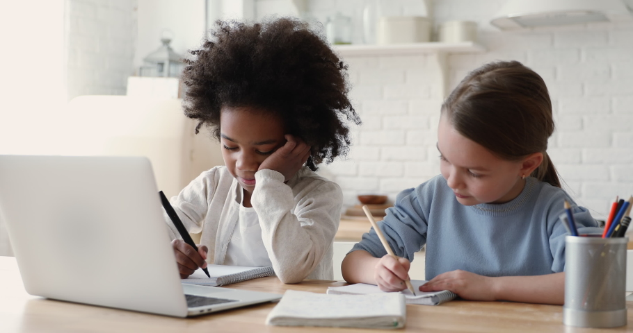 Cute primary school age girls of mixed race ethnicity studying together. African and caucasian sisters or friends doing homework writing exercise distance learning. Diverse children home education. Royalty-Free Stock Footage #1051329862