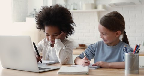 Cute primary school age girls of mixed race ethnicity studying together. African and caucasian sisters or friends doing homework writing exercise distance learning. Diverse children home education.