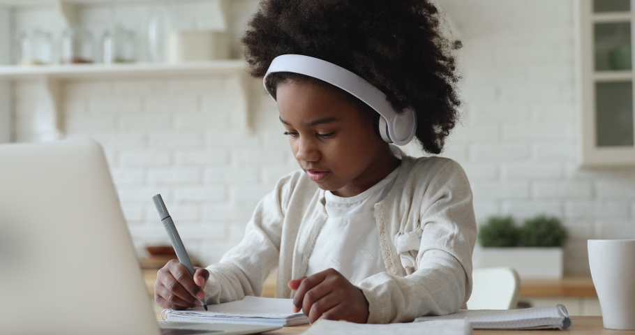 Afro american kid girl school pupil wearing headphones studying online from home watching web class lesson or listening tutor by video call elearning on pandemic isolation. Children remote education. | Shutterstock HD Video #1051329937