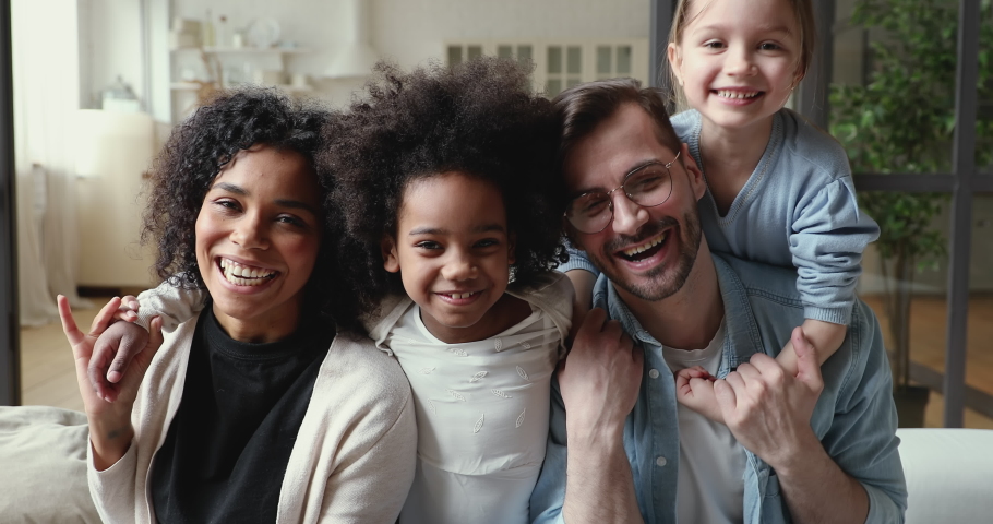 Happy mixed ethnicity family laughing, cuddling at home. Positive afro american mother, caucasian father and diverse kids daughters hugging on sofa together. Interracial parents and children portrait Royalty-Free Stock Footage #1051329946
