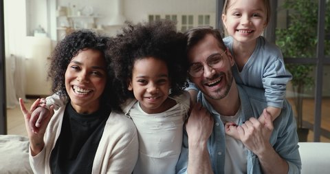Happy mixed ethnicity family laughing, cuddling at home. Positive afro american mother, caucasian father and diverse kids daughters hugging on sofa together. Interracial parents and children portrait
