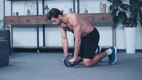 young shirtless sportsman training with fitness wheel on floor at home