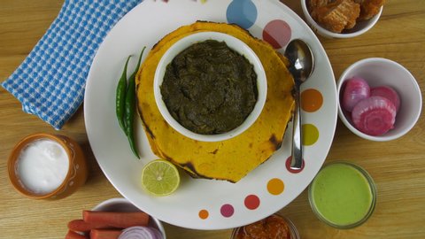 Closeup shot of woman hands adding butter to traditional Punjabi cuisine - Saag. Top view - Punjabi thali with Makki Ki Roti and Sarson ka saag served with Lassi, salad, pickle, mint chutney, and j...