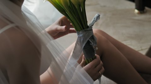 Bride's morning. Bride in lingerie and veil holding her wedding bouquet of white callas. Close up of female hands holding wedding bouquet of white callas.