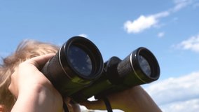 Closeup view video of cute white young kid looking through old black binoculars standing in sunny summer countryside landscape.