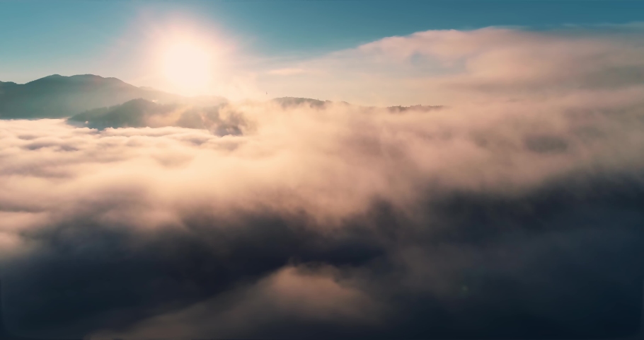 Flying over the clouds during morning sunrise in Carpathian Mountains. Above.Golden fluffy clouds moving softly on the sky and the sun shining through the clouds with beautiful rays and lens flare.	