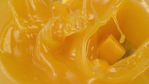 Mango chunks falling into mango juice in slow motion. .