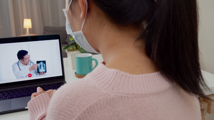 Slide Shot : Back view of asian woman video call with asian doctor at home. Patient girl listening lung x-ray result from doctor via video conference. Coronavirus and self isolation at home concept. | Shutterstock HD Video #1051361128
