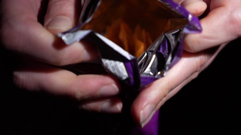 This slow motion video shows anonymous hands opening a bag of delicious tortilla cheese chips.
