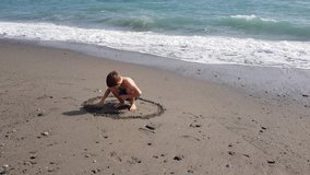 A beautiful cute child draws on the sand by the sea. Mobile phone video.
