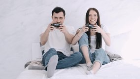 Beautiful young girl and boyfriend are playing video games. The couple is having fun together laying on bed.They are fighting, smiling and hugging.This is an interesting idea of quarantine activity.