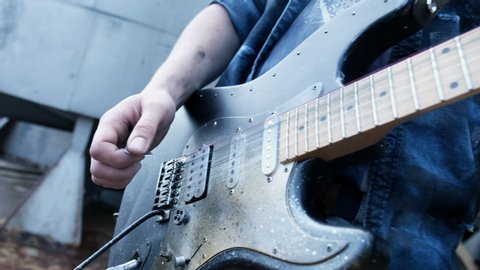 Cool man energy hand playing on string of guitar giving rock chord. Person creates mood music for concert emotion. Male play guitar abandoned place close up use electro acoustic music song 4K.