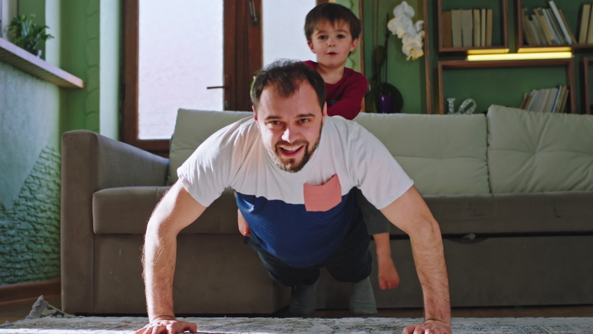 Funny little boy with his dad doing sport at home in living room at sunset dad doing hard push-ups with small boy on his back. Shot on ARRI Alexa Mini Royalty-Free Stock Footage #1051374268
