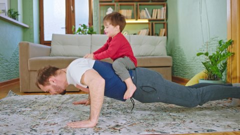 Sport time at home in the living room dad with his small cute son doing push-ups together while the small boy are on his back