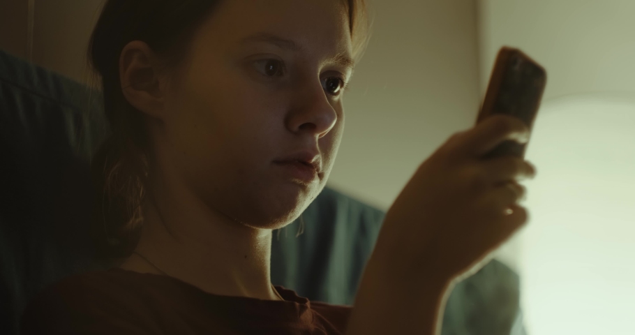 a girl uses a smartphone in a dark room, the screen illuminates her face