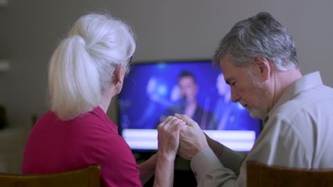 A mature couple worshiping as they attend virtual church by streaming the online platform to their television because congregation and group fellowship is restricted during COVID19 pandemic.