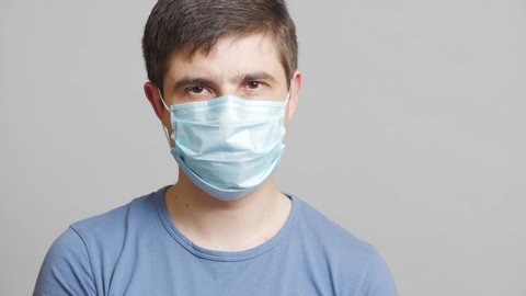 man with humor in surgical mask and sterile gloves on a gray background rubbing his hands slyly, concept medicine joke,strange doctor