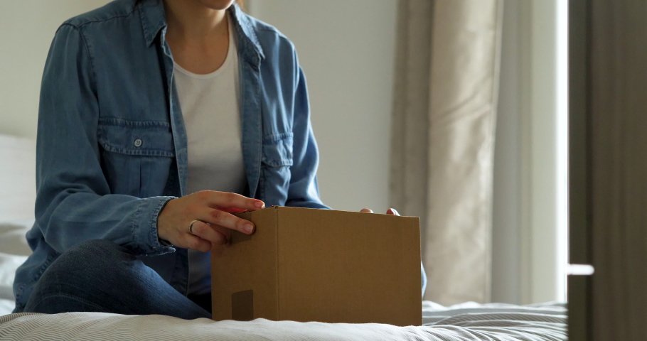 An young woman is excited while opening a package of a parcel delivered by mailman in her home. Concept: purchase, delivery, e-commerce, online shopping, emotions, client satisfaction, surprise Royalty-Free Stock Footage #1051376911