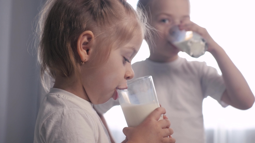 little girl and boy drink milk. happy family kids teamwork concept. children brother and sister drink milk from lifestyle a glass glass indoors morning breakfast Royalty-Free Stock Footage #1051377904