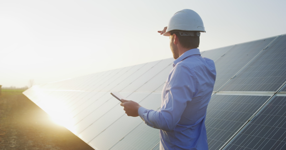 An young engineer is checking with tablet an operation of sun and cleanliness on field of photovoltaic solar panels on a sunset. Concept:renewable energy, technology,electricity,service, green,future  | Shutterstock HD Video #1051378879