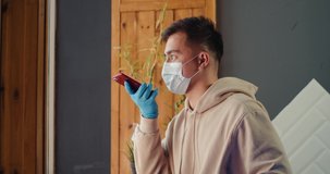 Young asian man send voice audio message with phone wearing protective mask on a phone video call in hospital, standing by a window, coronavirus isolation.