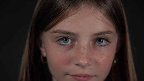 Beautiful blond young girl with freckles indoors on a black background, close up portrait