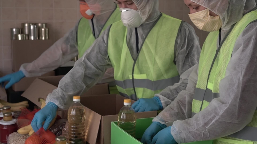 Muslim Charity - Donate Zakat and Sadaqah during Ramadan  and Covid-19. Volunteers in protective suits, gloves and masks collect a box of food. Food banks feeding needy, indigent lockdown people  Royalty-Free Stock Footage #1051386097