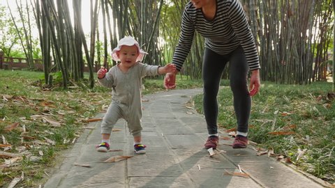 Lovely little asian baby girl take first step walking in the bamboo garden outdoor at spring afternoon slow motion 4k footage of baby development footage kid learning to walk fall to the ground
