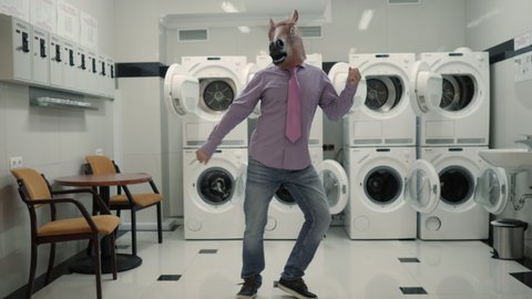 Joyful Man in mask horse Dancing Cheerful In Laundry Room. Man Dancing Viral Dance And Have Fun In Laundry Room. Happy Guy Enjoying Dance, Having Fun Together, Party Halloween. Slow Motion. Halloween