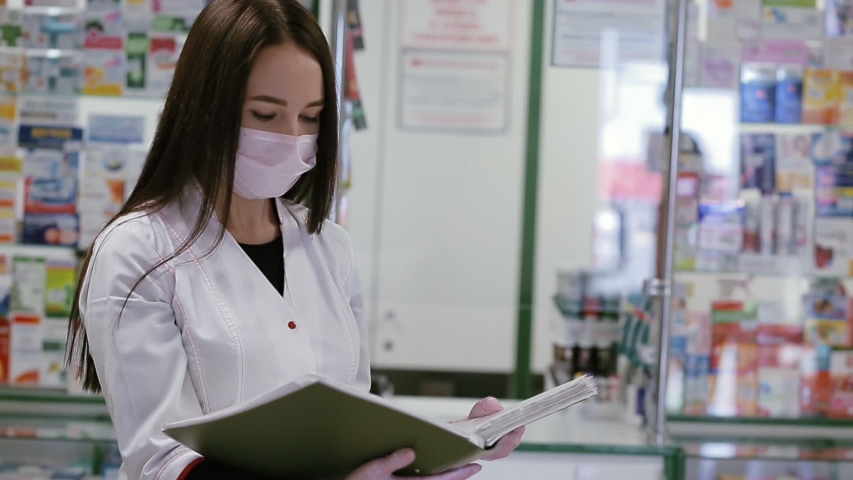 A woman in a medical mask and dressing gown reads papers in a folder, and then communicates with a woman who has approached her. Concept of a viral pandemic and protection against infection Royalty-Free Stock Footage #1051396795