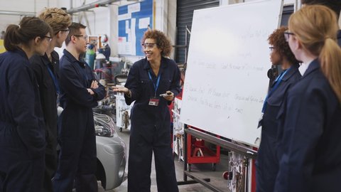 Female tutor by whiteboard with students teaching auto mechanic apprenticeship at college - shot in slow motion