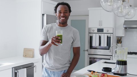 Portrait of man wearing pyjamas standing in kitchen drinking freshly made fresh fruit and vegetable smoothie - shot in slow motion