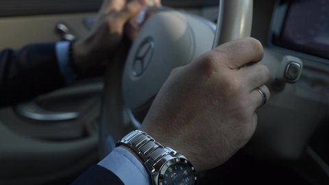 Kyiv, Ukraine. Oct 2018. Close-up Male Hands Turn Steering Wheel of Luxury Business Car Mercedes Benz S Class. Young Successful Businessman Confident Driving on Urban Highway, City Street. Bright Day
