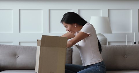 Side view young excited female asian ethnicity client unpacking huge cardboard parcel. Happy millennial vietnamese woman unboxing order from internet store, satisfied with fast delivery service.
