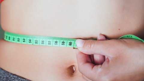Young athletic slim woman measuring her waist. A girl measures her waistline with a centimeter tape. Healthy lifestyle and proper nutrition. Diet for weight loss. Close up.