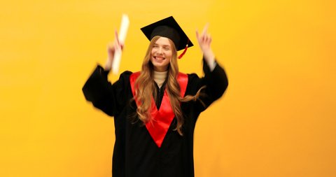 graduate girl with a diploma, shows a gesture of victory and success, on a yellow background, celebrating graduation from the University, dancing, party