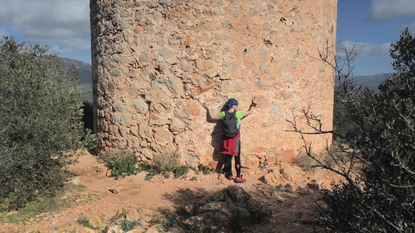 Woman gives hug defense tower torre de Cap Andritxol, Mallorca, Spain. Trail along west shore of island.