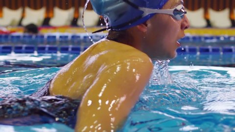 Side view of professional female swimmer in goggles on swimming pool . Woman swimmer dive in water pool . Girl swimming underwater in the large pool . Close up , slow motion .